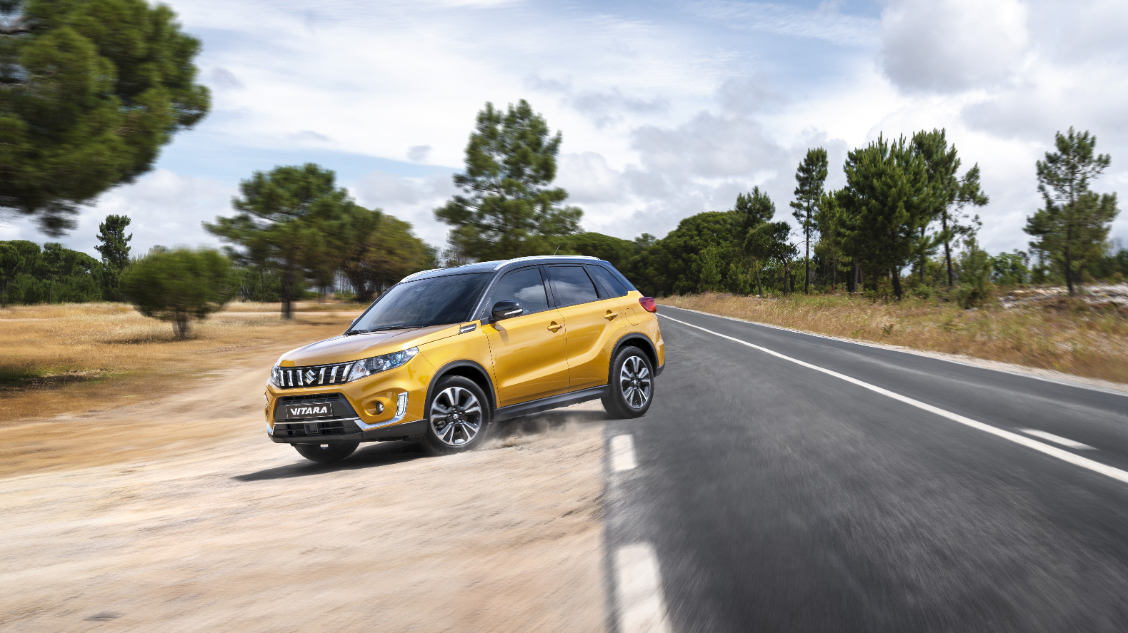 A mustard colored Suzuki Vitara on a dirt road.
